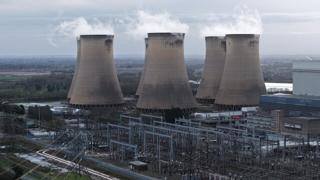 Aerial view of colossal cooling towers release plumes into the grey sky above the industrial landscape, Drax Power Station, Selby, United Kingdom.