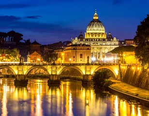 Fototapeta premium Illuminated cityscape at dusk, featuring a domed structure and arched bridge reflecting in calm water. The night sky is deep blue