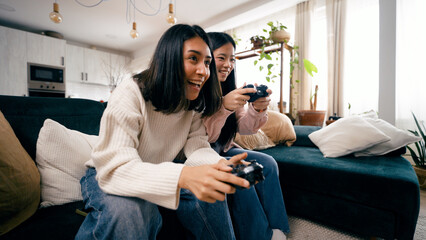 Two friends sitting on a sofa, happily gaming with controllers in a cozy living room, enjoying a fun time © DMegias
