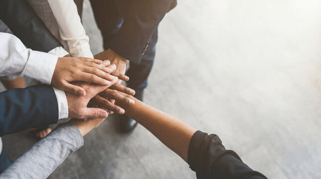 A close-up overhead view of a diverse team's hands stacked together in a gesture of unity, collaboration, and support.