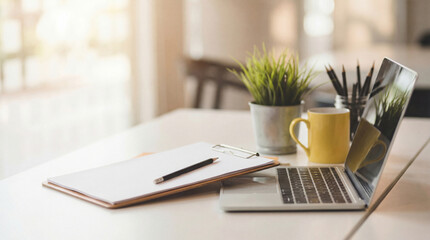 A clean and organized home office desk setup with a laptop, notebook, pencil, and a small potted plant, illuminated by natural light. © Jonathan