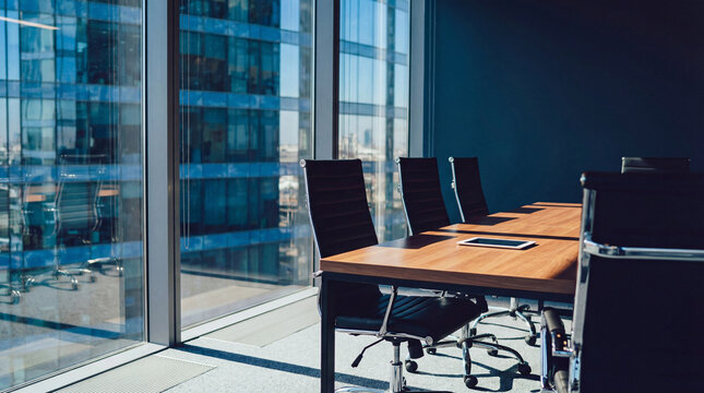 Modern office meeting room with large windows overlooking a cityscape, featuring a conference table and chairs with a tablet device, perfect for corporate presentations and business discussions.