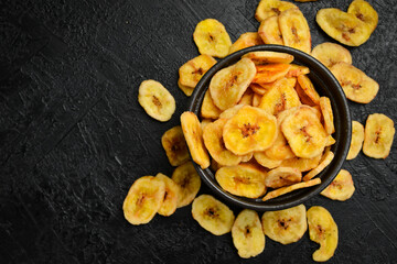 Banana chips. Dried banana slices in a black ceramic bowl. Top view. © Yaruniv-Studio
