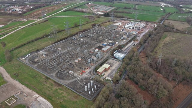 Aerial view of the National Grid Hams Hall Substation, a stark contrast of industrial gray against the surrounding verdant fields, Birmingham, United Kingdom.