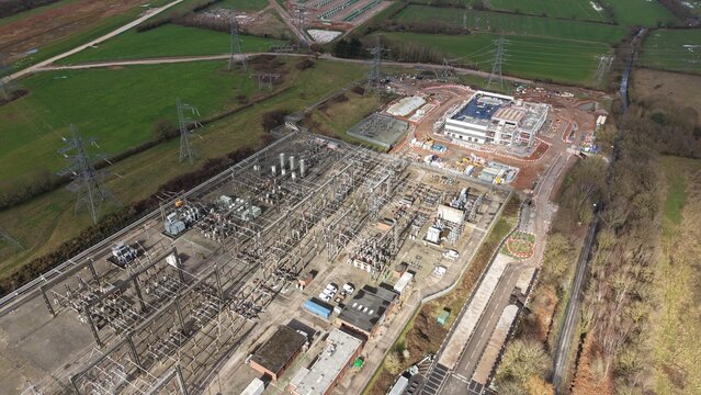 Aerial view of the National Grid Hams Hall Substation sprawling with complex infrastructure against a backdrop of green fields, Birmingham, United Kingdom.