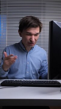 Vertical video stressed man with frustrated expression and raised hand reacting to an issue on his computer monitor, showing common office work problems and technology errors