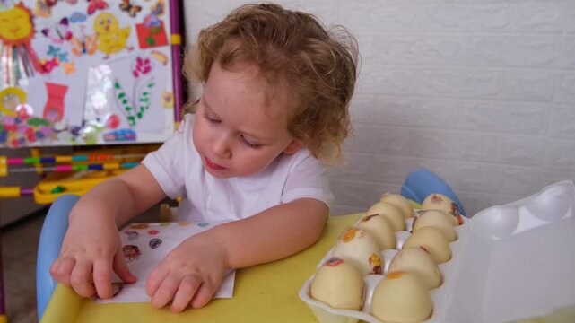 Moscow, Russia, 12.04.2025 Young caucasian boy playing with easter eggs and stickers, decorating eggs for a spring holiday celebration with a child