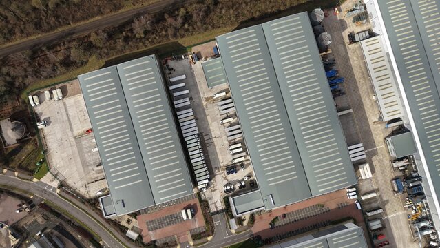 Aerial view of the expansive distribution center, a symphony of silver roofs contrasting with the earthy tones of the surrounding landscape, Birmingham, England, United Kingdom.