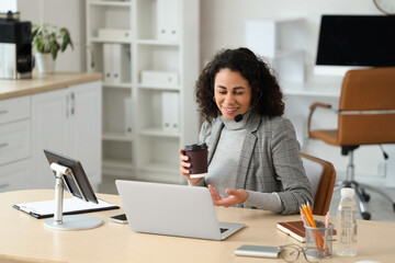 Obraz premium Female African-American online business consultant with coffee at desk in office