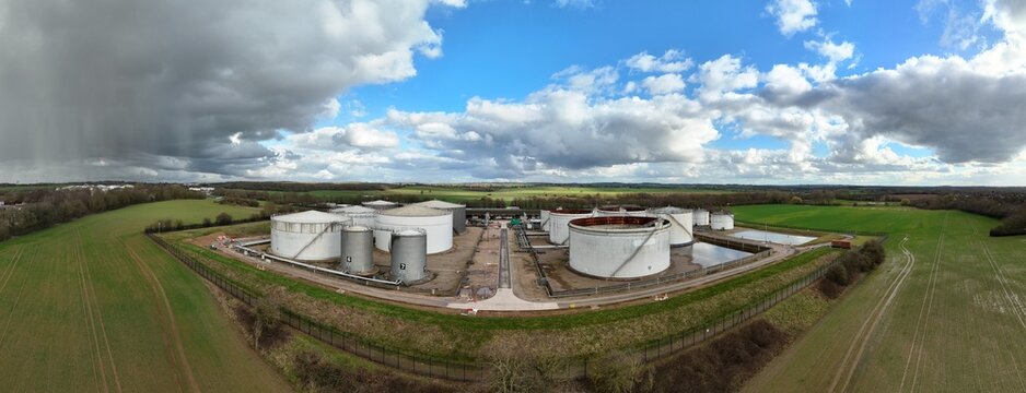 Aerial view of cylindrical white oil tanks contrast against the green fields under a sky of dark storm clouds and patches of blue, Kingsbury, Tamworth, United Kingdom.