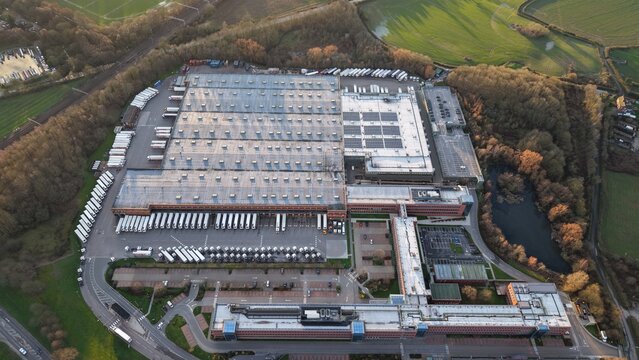 Aerial view of the expansive ALDI UK & Ireland National Head Office complex, where geometric roofs meet the organic curves of surrounding trees, Atherstone, United Kingdom.