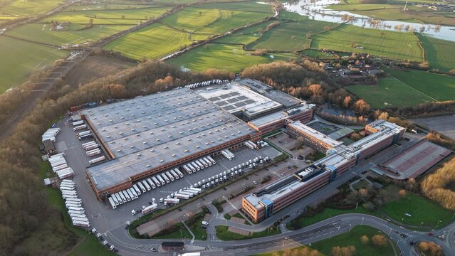 Aerial view of the ALDI UK & Ireland National Head Office, a vast complex of buildings and parked trucks nestled amidst verdant fields and trees, Atherstone, United Kingdom.