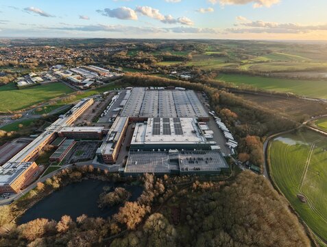 Aerial view of the ALDI UK & Ireland National Head Office, a sprawling complex of buildings and parking lots, nestled amidst a tapestry of green fields and autumnal trees, Atherstone, United Kingdom.