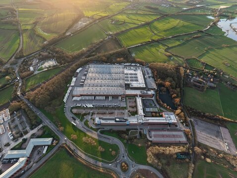 Aerial view of the sprawling ALDI UK & Ireland National Head Office complex, a symphony of gray roofs amidst verdant fields and winding roads, Atherstone, United Kingdom.