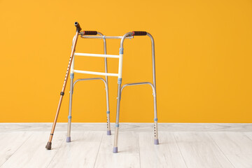 Medical walker with stick near orange wall
