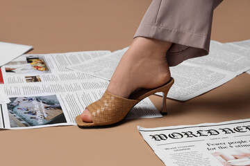 Naklejka premium Leg of woman in high heels with many newspapers on brown background