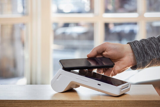 Payment Terminal. Contactless Mobile Payment at POS Terminal. Hand Holding Smartphone over Modern Point-of-sale Terminal. Mobile Electronic Payment Terminal.