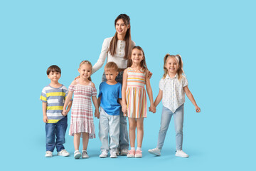 Fototapeta premium Young female teacher or babysitter standing with group of preschool children holding hands and smiling isolated on blue background