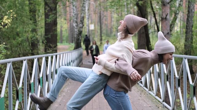 Two girlfriends are walking and having fun outside among autumn trees in a city park.