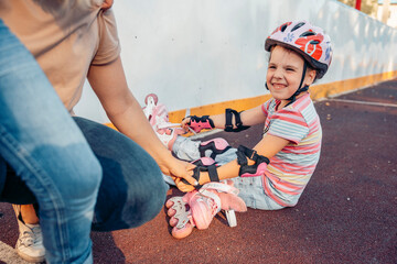 Naklejka premium young Caucasian girl sits on the ground, putting on pink roller skates. An adult woman assists her nearby. enjoying quality time together outdoors