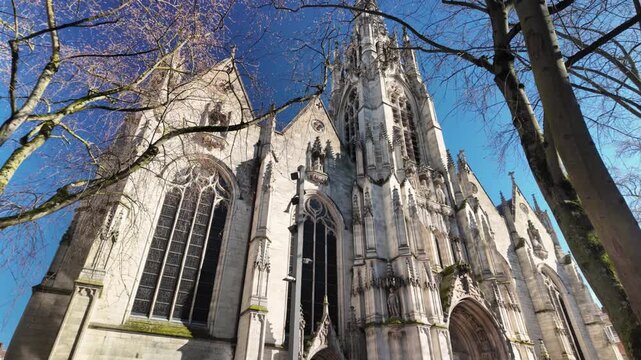 Slow tilt up shot of Saint Maurice Church in Lille, showcasing Gothic facade and historic stone detail under clear blue sky.