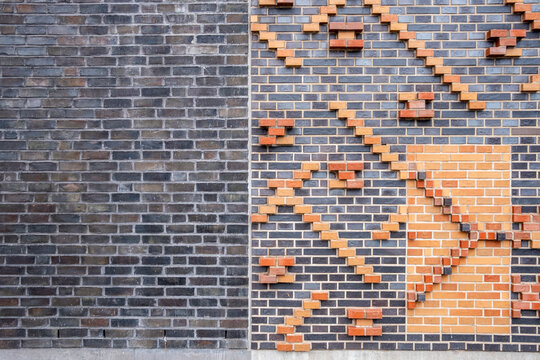 Brick facade wall showing abstract geometry relief pattern and textured design with orange accents forming a bold architectural surface