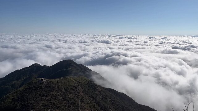 A breathtaking 1080p aerial time-lapse showcasing a thick, white sea of clouds rolling and flowing like ocean waves over dark mountain ridges under a clear sky, Sichuan, China.