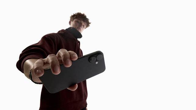 Low angle young man holding smartphone toward camera isolated on white background. Concept of mobile app promotion, fintech services, mobile payments and digital technology advertising.