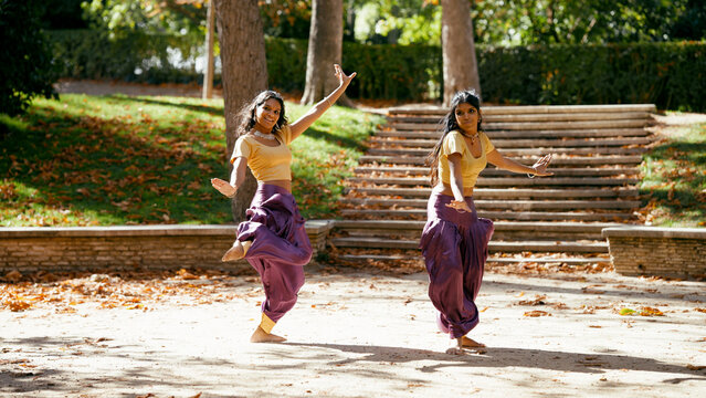 Two indian women performing classical indian dance, displaying culture and elegance outdoors during autumn with colorful traditional costume