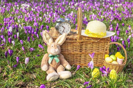 Easter time when the  clocks go forward in Springtime with an Easter Bunny, colourful eggs, chicks and Easter bonnet on a traditional wicker picnic basket and alarm clock.  Horizontal. Copy space