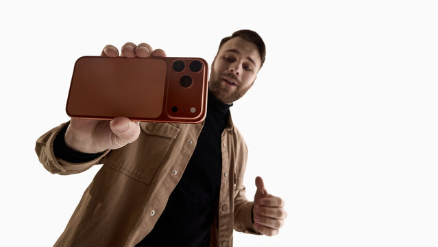 Man presenting smartphone toward camera from low angle isolated on white background. Concept of product review, tech blogging, influencer marketing, gadget promotion and mobile device advertising.