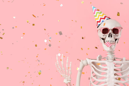 Human skeleton in party hat and sunglasses on pink background, closeup