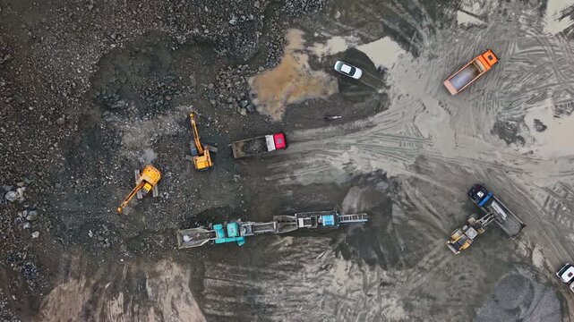 Workers operate heavy machinery in a granite quarry. Trucks and equipment move around the site, showing active mining and processing of granite material.