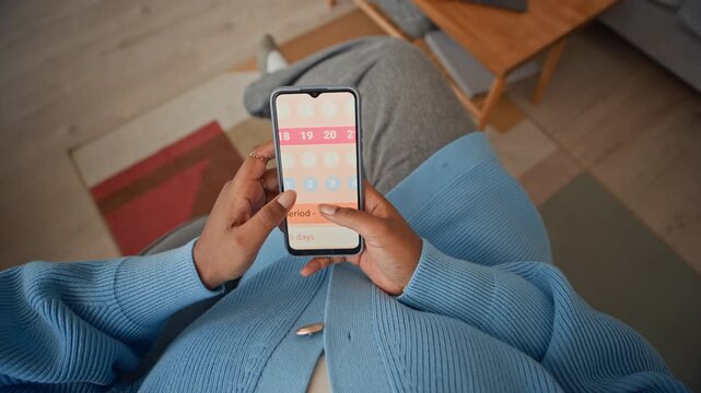 Top cropped shot of unrecognizable woman checking menstrual period in app on smartphone while sitting in living room
