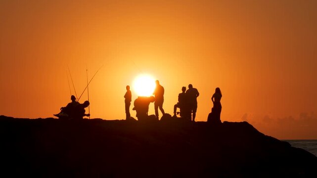 People fishing with a fishing rod at sunset. Impressive image of red sky and sun.