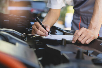 Obraz premium Auto check up and car service shop concept. Mechanic writing job checklist to clipboard to estimate repair quotation to client at workshop garage.