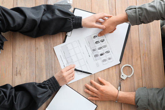 Female police officer taking fingerprints from suspect with handcuffs on table, top view