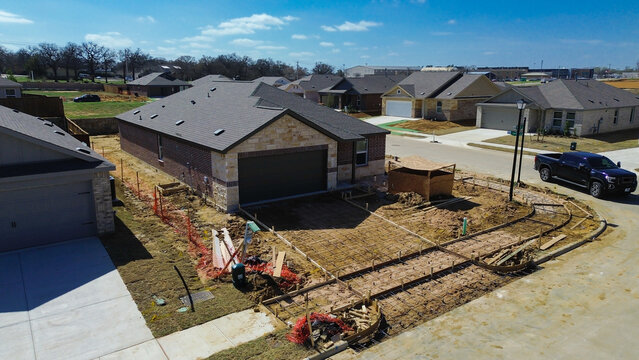 Driveway construction underway at new home corner house along Arabian Ln near Highpointe Ranch by US-377, Blackjack Rd. Dark shingles, brick textures, rebar lined concrete forms in Aubrey, Texas