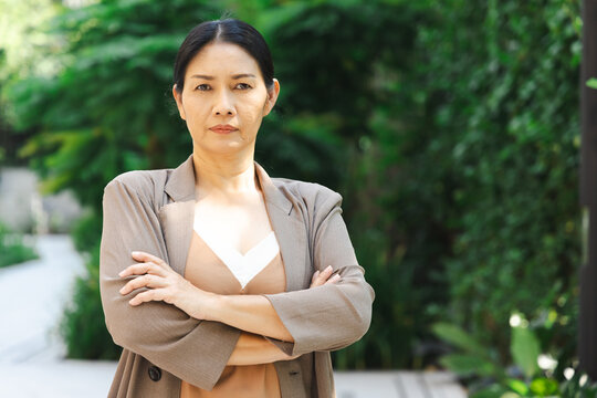 Serious and stressed middle aged asian woman with negative expression in summer green urban park