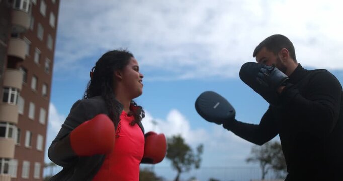 Personal trainer doing boxing exercise with curvy african girl outdoor - Sport, coach, workout and diet concept 