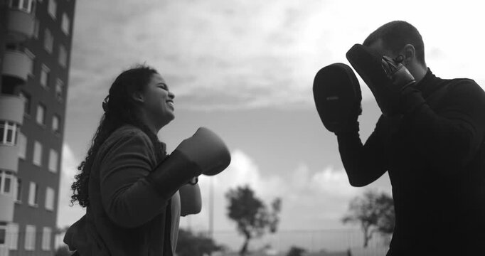 Curvy african american girl having fun doing boxing exercise with personal trainer outdoor - Sport, diet and plus size people concept - Black and white editing