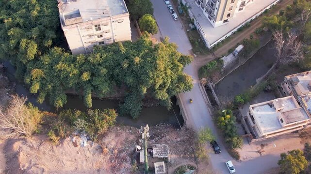 Aerial shot of a narrow stream beside residential buildings and trees with nearby roads, Islamabad, Pakistan
