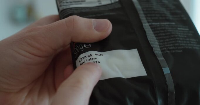 Close-up of a hand pointing at the expiration date on packaged food, emphasizing product safety and consumer awareness.