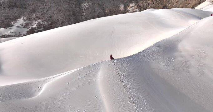 Aerial view of pristine white sand dunes, adorned with tiny figures in red, contrasting against the rugged, rocky terrain, Socotra.