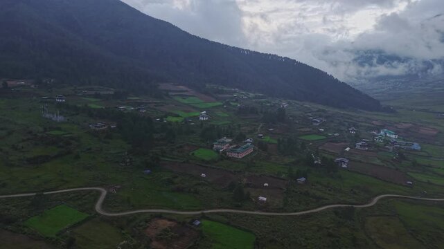 Aerial view of the Phobjikha Valley showcasing the green fields and scattered buildings nestled beneath the clouds, Nubding, Bhutan.