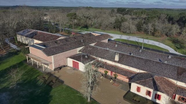 Chateau de Malleret, France - 06 January 2026: Aerial view of the Chateau with red doors and tiled roof surrounded by green lawns and a backdrop of bare trees.