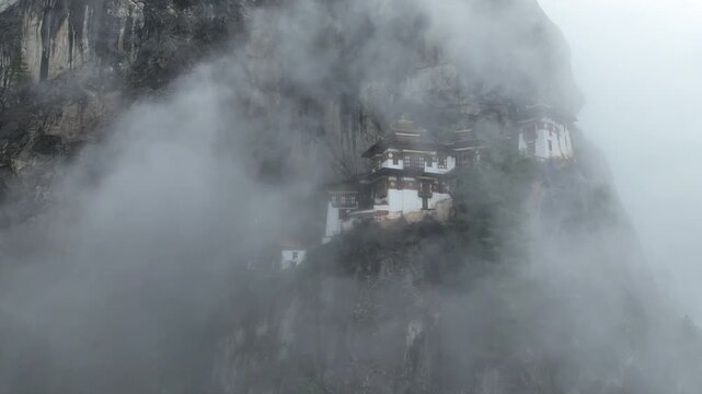 Aerial view of Tiger's Nest Monastery perched dramatically on a cliffside, shrouded in ethereal mist and clouds, Taktsang, Paro, Bhutan.