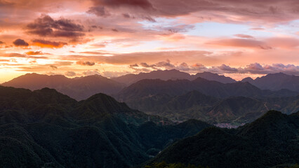 Fototapeta premium A breathtaking aerial panorama of lush green mountain ranges stretching into the horizon under a dramatic, colorful sunset sky with vibrant clouds.