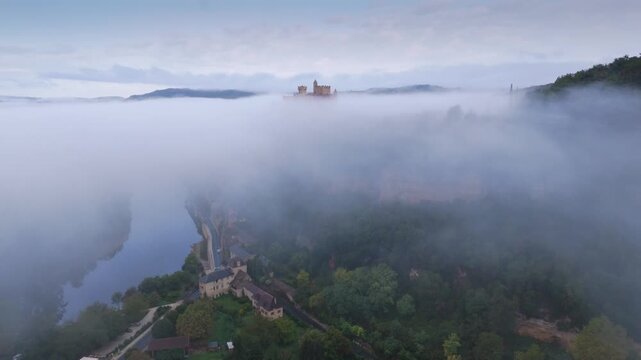 Beynac-et-Cazenac, France - 12 September 2025: Aerial view of Chateau Beynac piercing through a blanket of ethereal mist, amidst lush greenery.