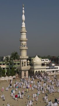 Aerial view of a gathering of people in white in front of a mosque with a tall minaret and a white dome, Malda, West Bengal, India.